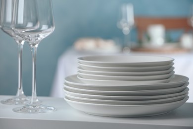 Photo of Stacked clean dishes and glasses on white shelf indoors