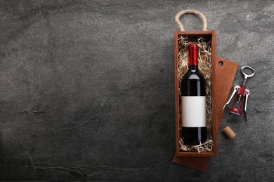 Bottle of wine in wooden box, cork and corkscrew on dark textured table, flat lay. Space for text