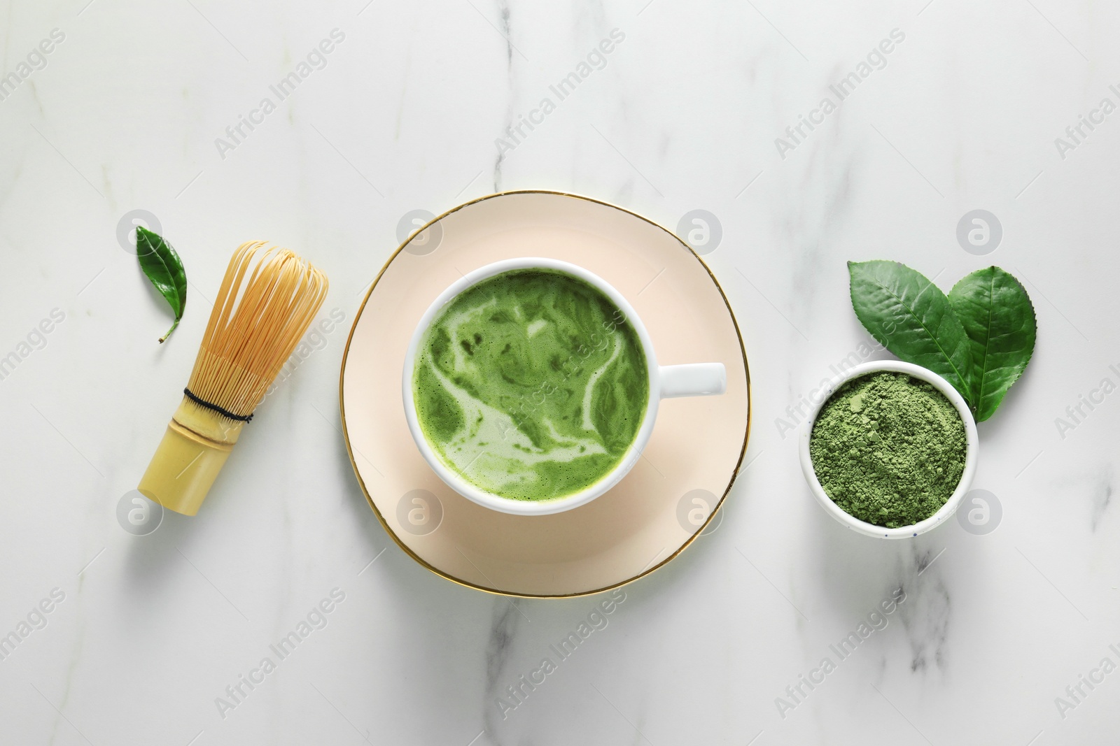 Photo of Cup of fresh matcha latte, powder and bamboo whisk on white marble table, flat lay