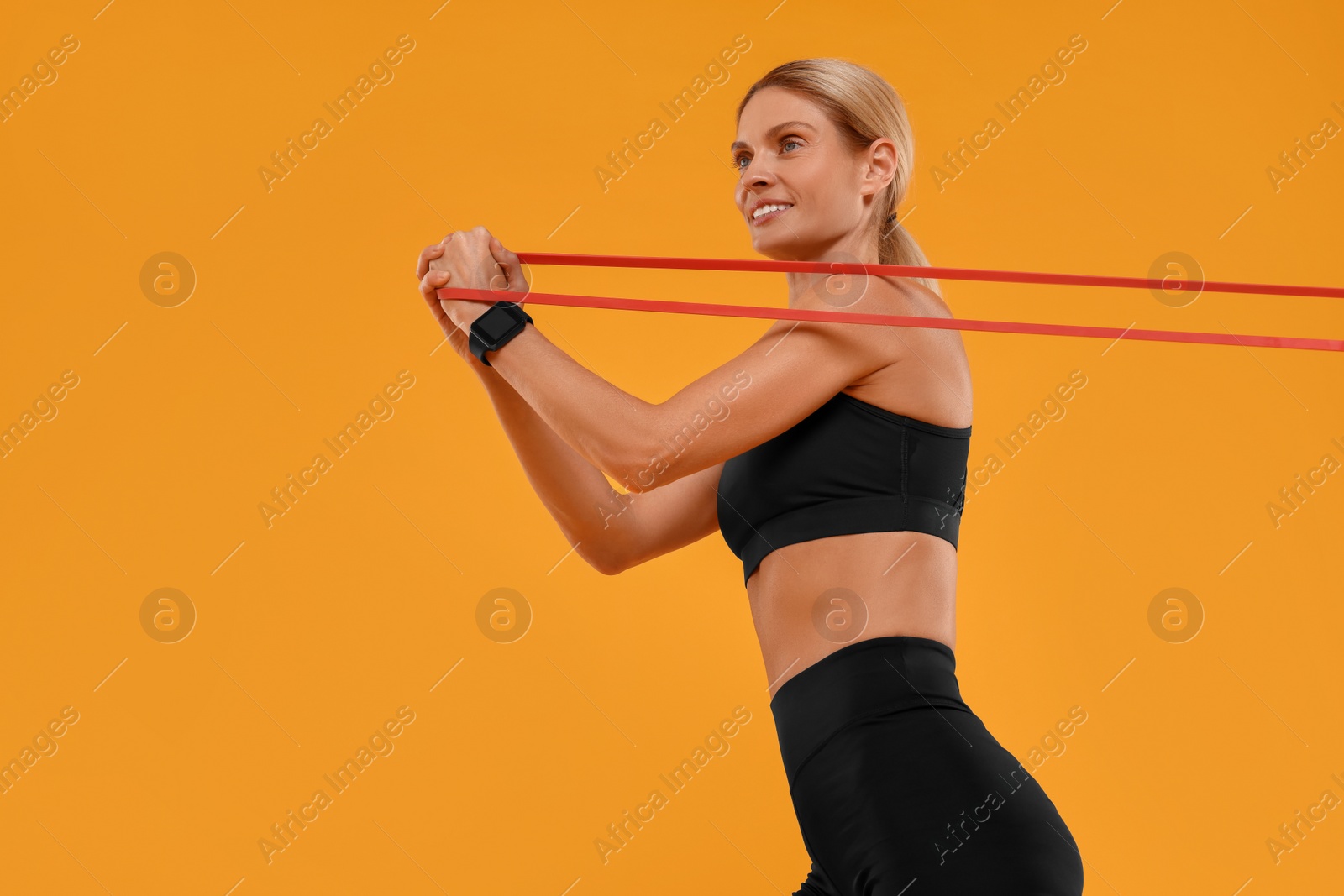 Photo of Woman exercising with elastic resistance band on orange background, low angle view