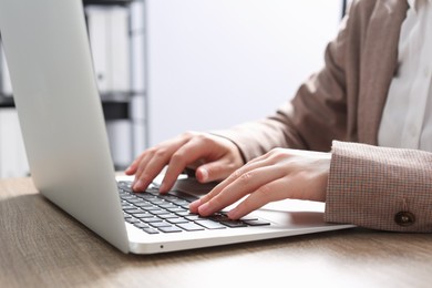 Photo of Woman working on laptop at wooden table in office, closeup