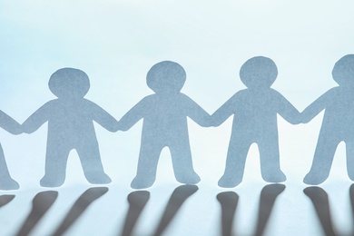 Photo of Paper people holding hands on light background. Unity concept