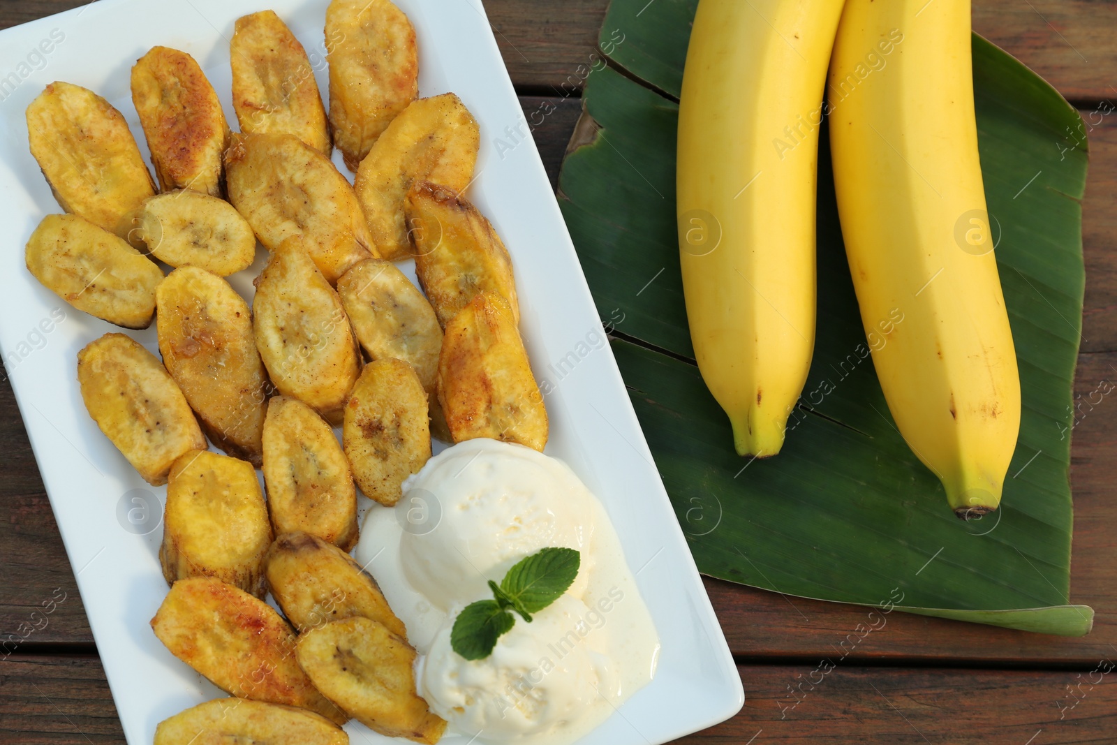 Photo of Tasty deep fried banana slices with ice cream and fresh fruits on wooden table, flat lay