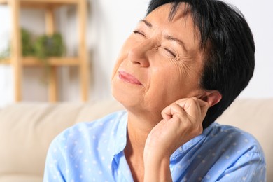 Photo of Senior woman suffering from ear pain at home, closeup. Space for text