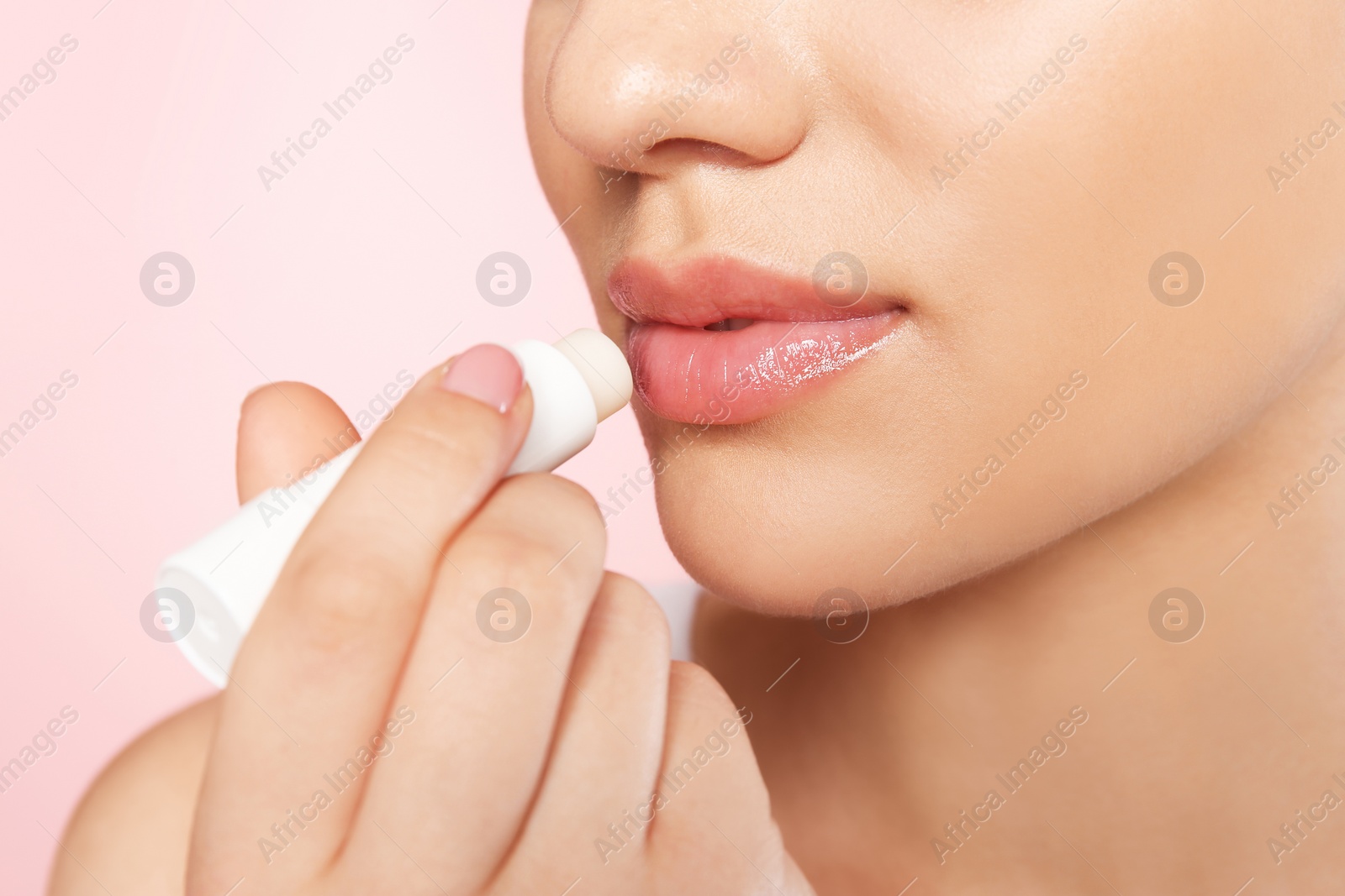 Photo of Young woman applying balm on her lips against color background, closeup