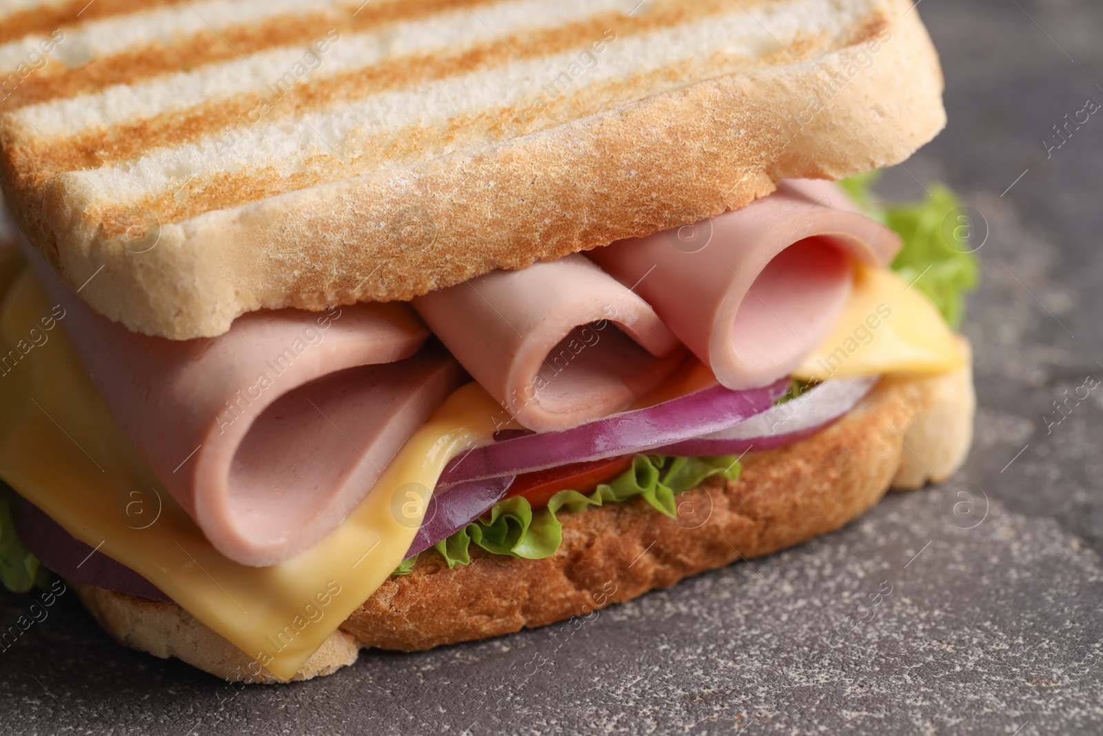 Photo of Delicious sandwich with boiled sausage, cheese and onion on grey textured table, closeup