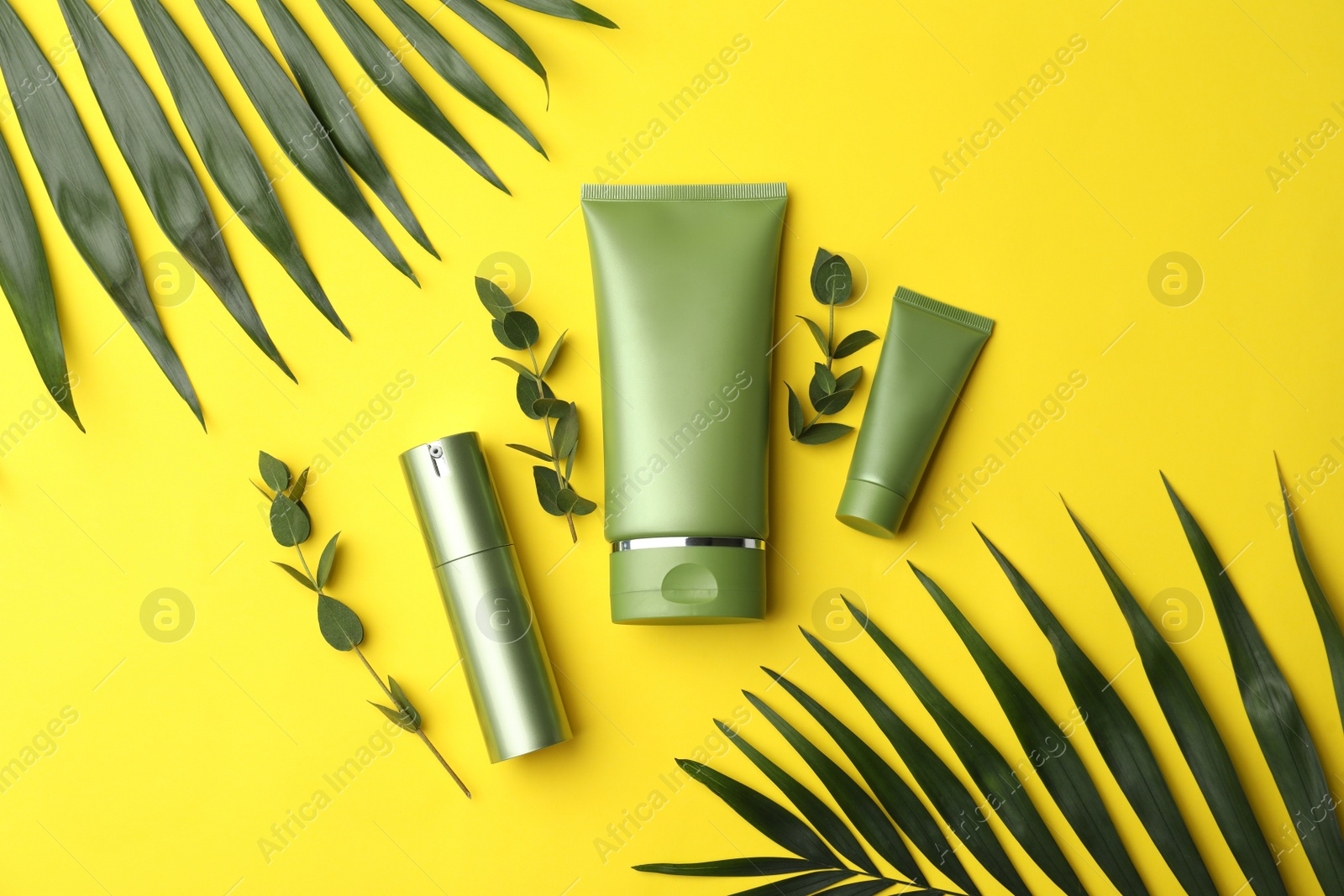 Photo of Set of cosmetic products and green leaves on yellow background, flat lay