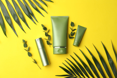 Set of cosmetic products and green leaves on yellow background, flat lay