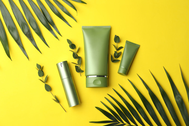 Photo of Set of cosmetic products and green leaves on yellow background, flat lay