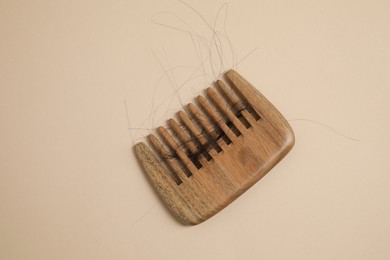 Wooden comb with lost hair on beige background, top view