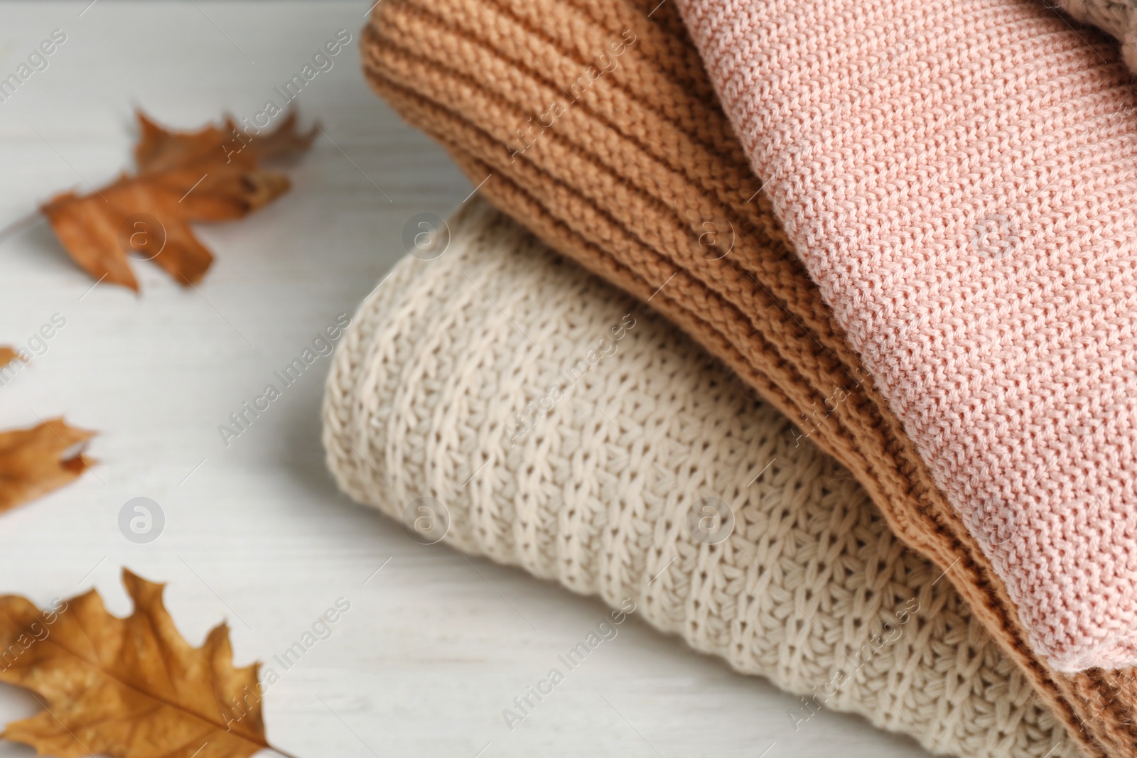 Photo of Stack of folded knitted sweaters and autumn leaves on table, closeup