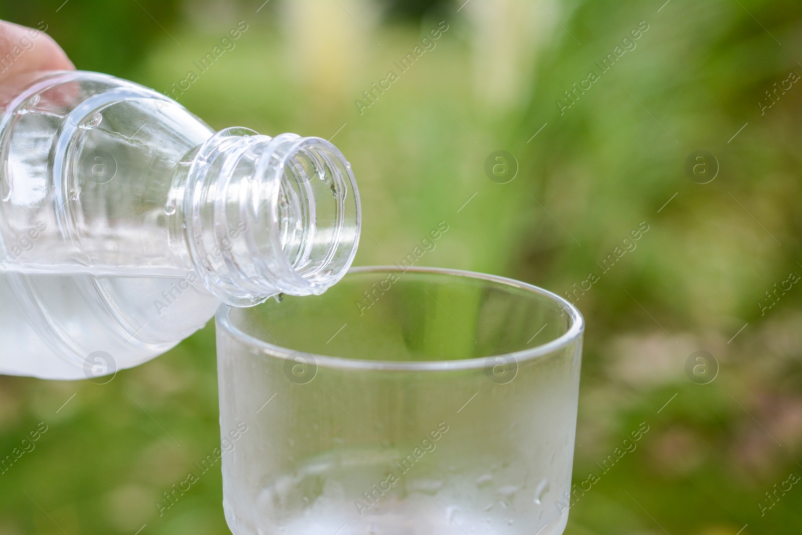 Photo of Woman pouring water from bottle into glass outdoors, closeup