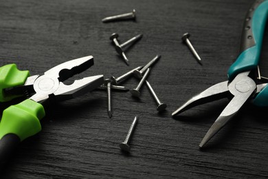 Pliers and nails on black wooden table, closeup