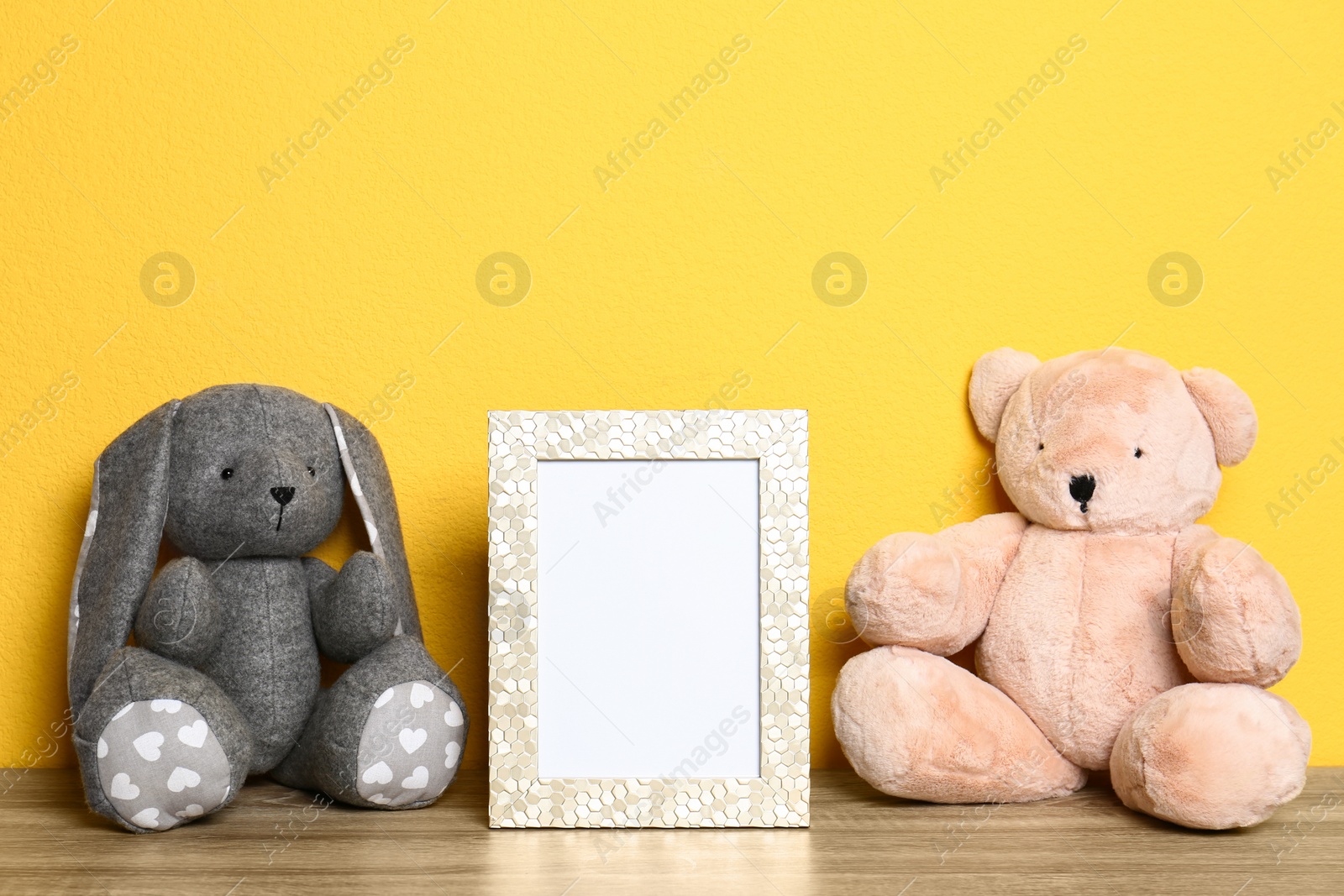 Photo of Soft toys and photo frame on table against yellow background, space for text. Child room interior