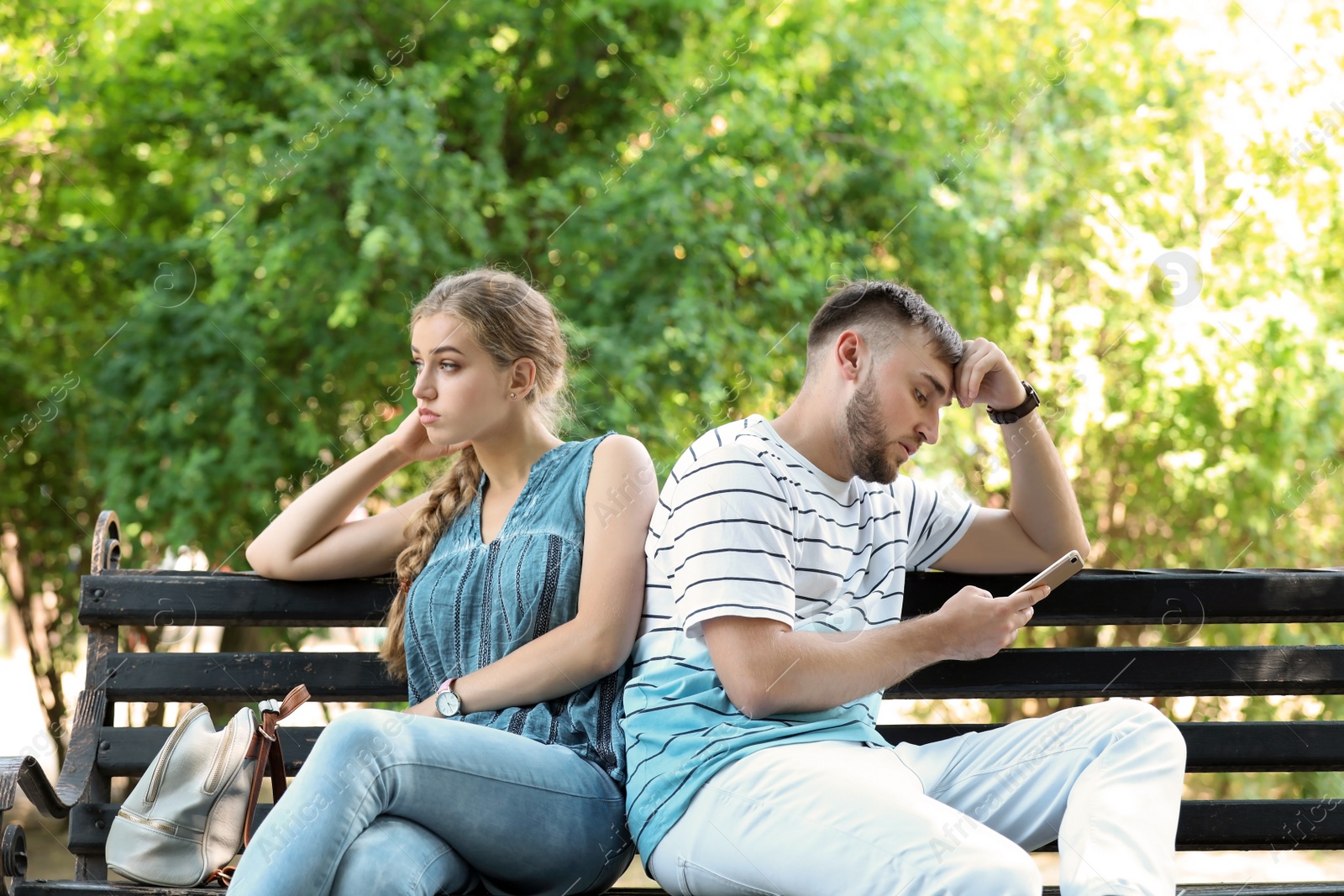 Photo of Young couple arguing while sitting on bench in park. Problems in relationship