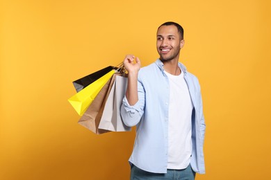 Photo of Happy African American man with shopping bags on orange background