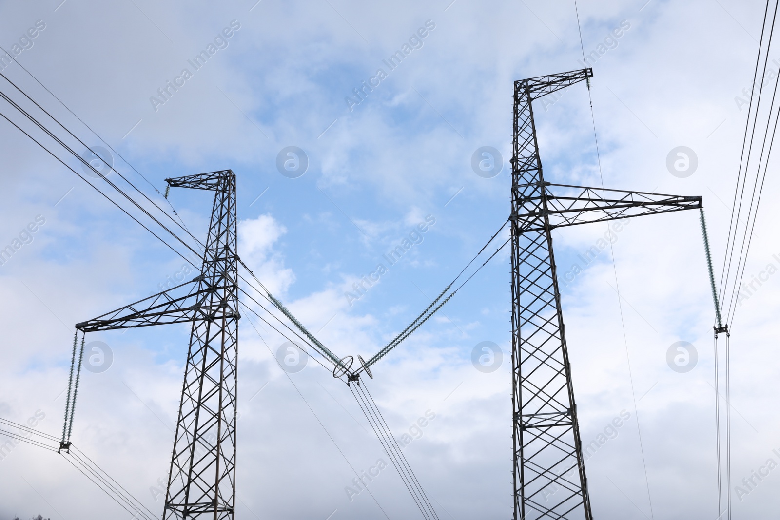 Photo of High-voltage towers with electricity transmission power lines against blue cloudy sky