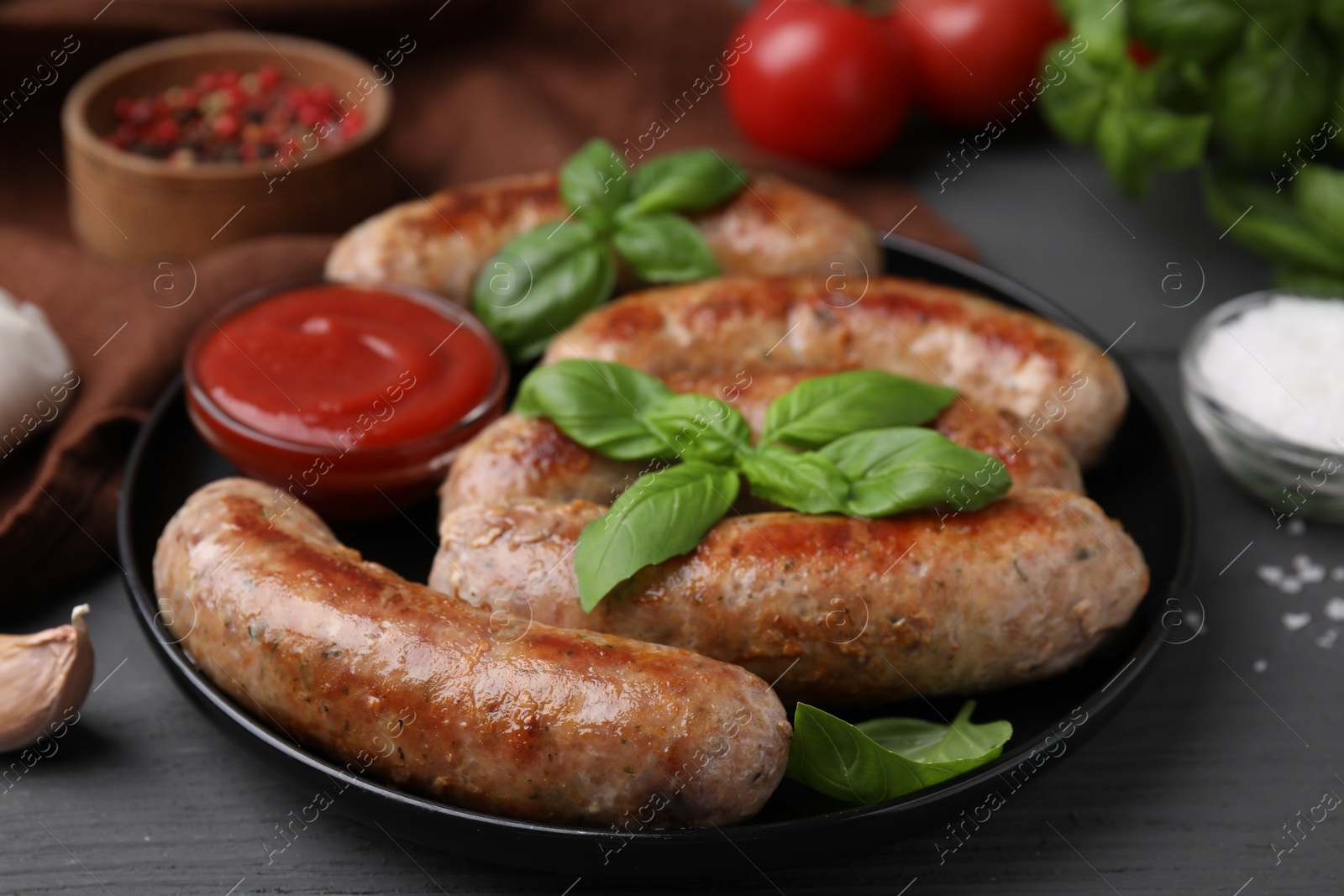 Photo of Tasty homemade sausages, ketchup and basil leaves on grey wooden table, closeup