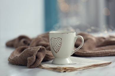 Photo of Delicious morning coffee, newspaper and knitted sweater on white table indoors