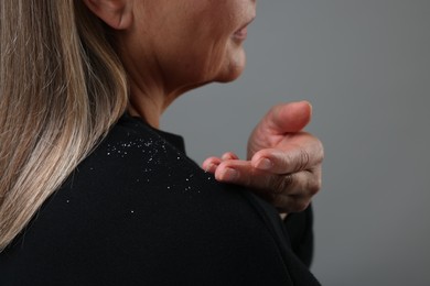 Photo of Woman brushing dandruff off her sweater on gray background, closeup