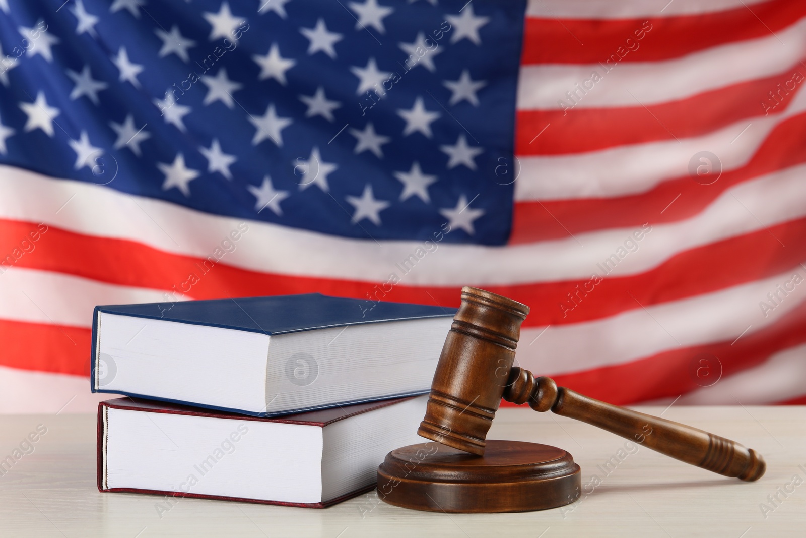 Photo of Judge's gavel and books on white wooden table against American flag