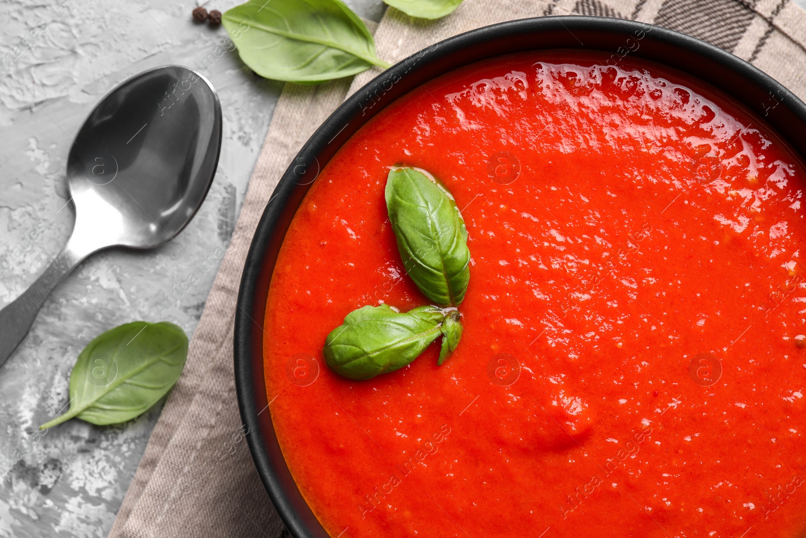 Photo of Delicious tomato cream soup served on grey textured table, flat lay