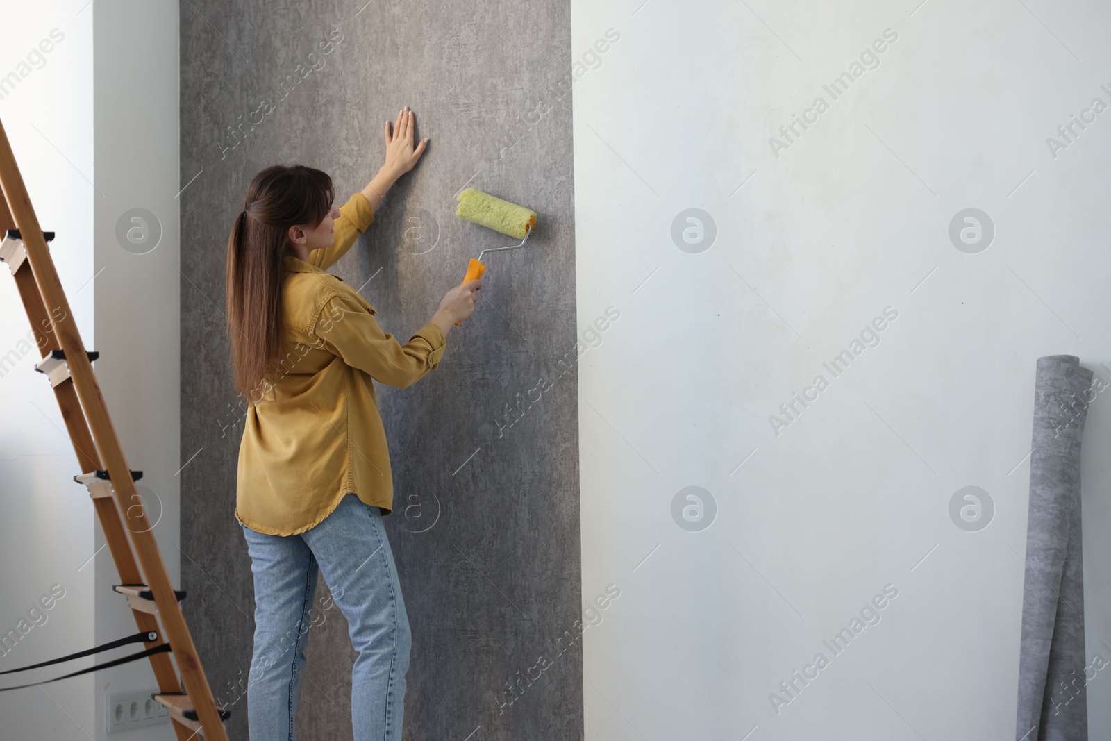 Photo of Woman hanging stylish gray wallpaper in room