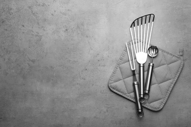 Photo of Different kitchen utensils and potholder on grey background, top view with space for text