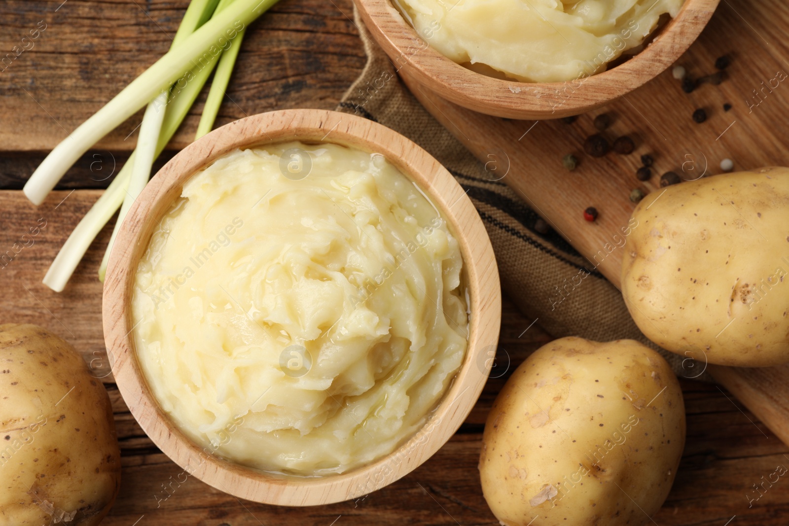 Photo of Bowls of tasty mashed potato, pepper and leeks on wooden table, flat lay