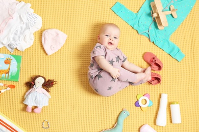 Cute little baby with clothing and accessories on color blanket, top view