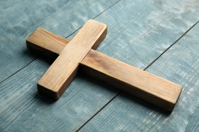 Photo of Christian cross on light blue wooden background, closeup. Religion concept