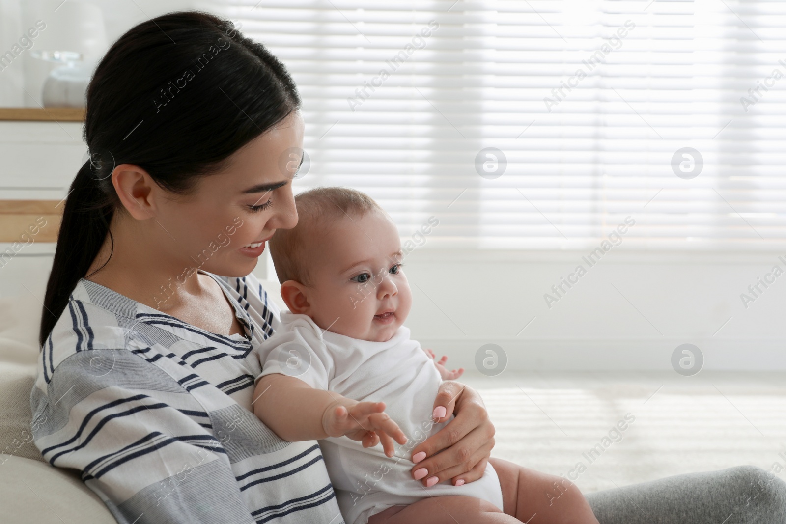 Photo of Young mother with her little baby on sofa at home, space for text