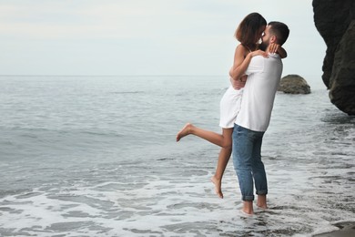 Young couple kissing on beach near sea. Space for text