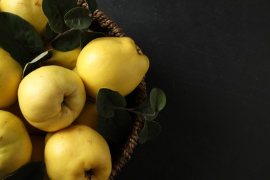 Photo of Fresh ripe organic quinces with leaves in wicker basket on black table, closeup. Space for text
