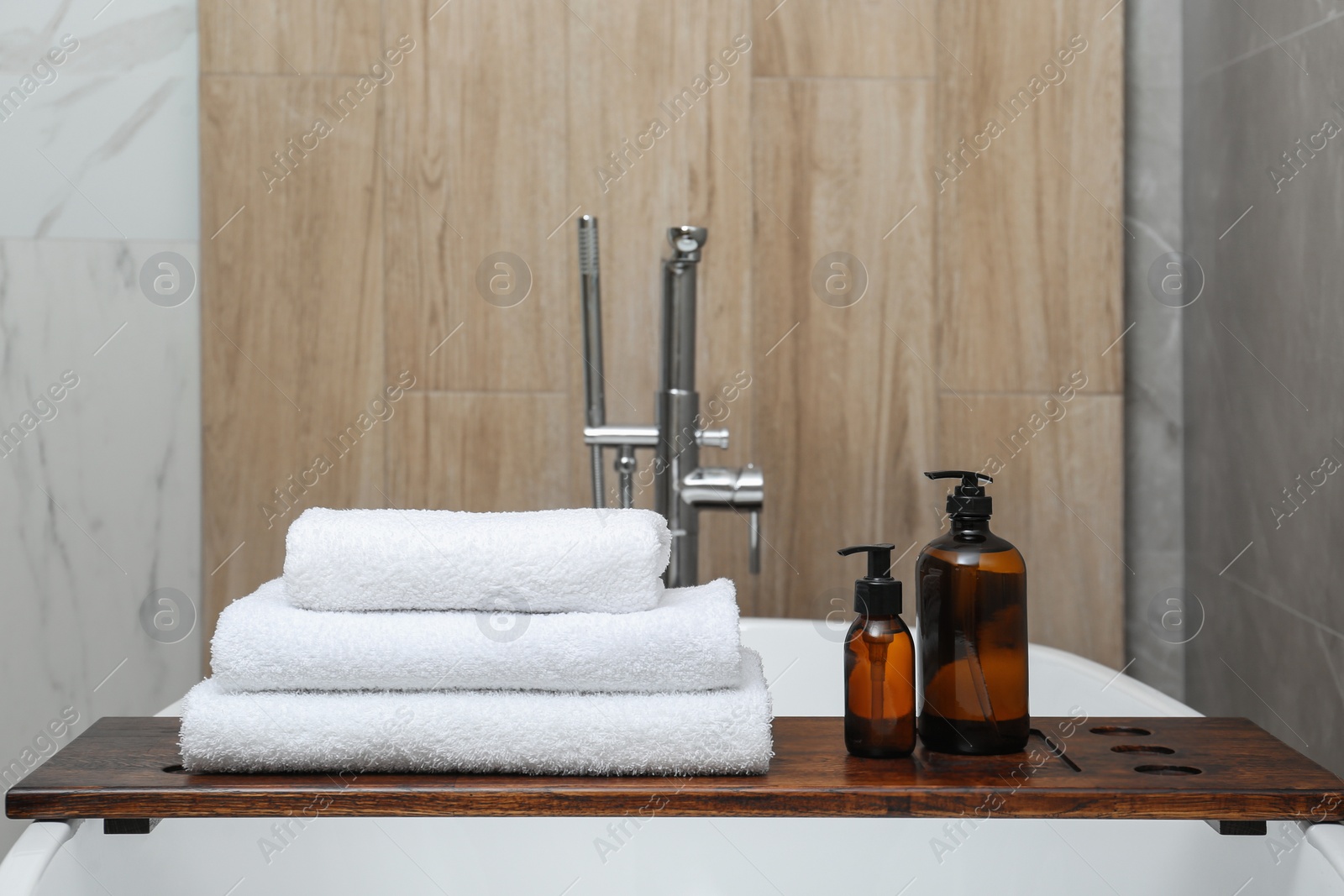 Photo of Stacked bath towels and personal care products on tub tray in bathroom