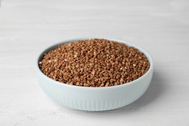 Photo of Uncooked buckwheat in bowl on wooden table