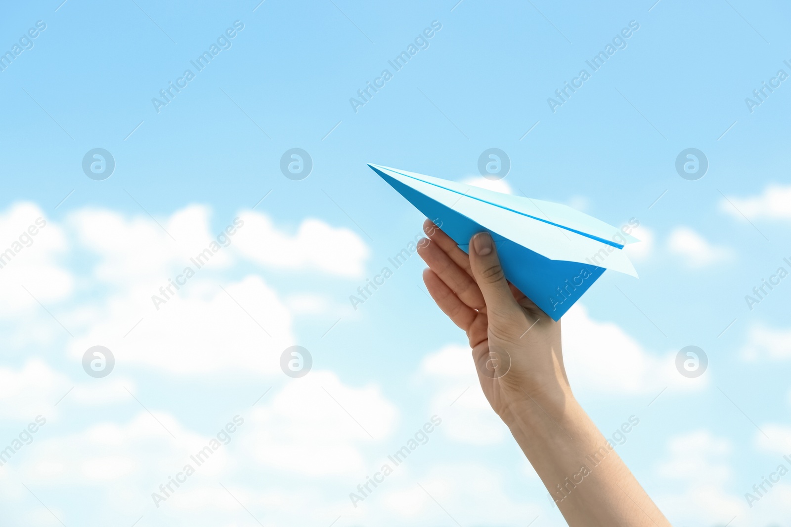 Photo of Woman holding paper plane against blue sky, closeup. Space for text