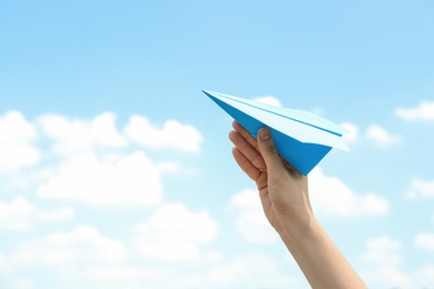 Photo of Woman holding paper plane against blue sky, closeup. Space for text