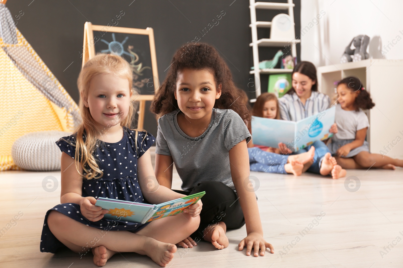 Photo of Cute little children reading book on floor in kindergarten, space for text. Indoor activity