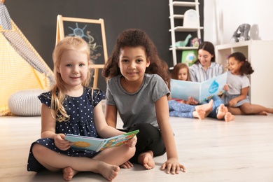 Photo of Cute little children reading book on floor in kindergarten, space for text. Indoor activity