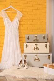 Storage trunks, gift box and beautiful wedding dress near yellow brick wall indoors. Interior design