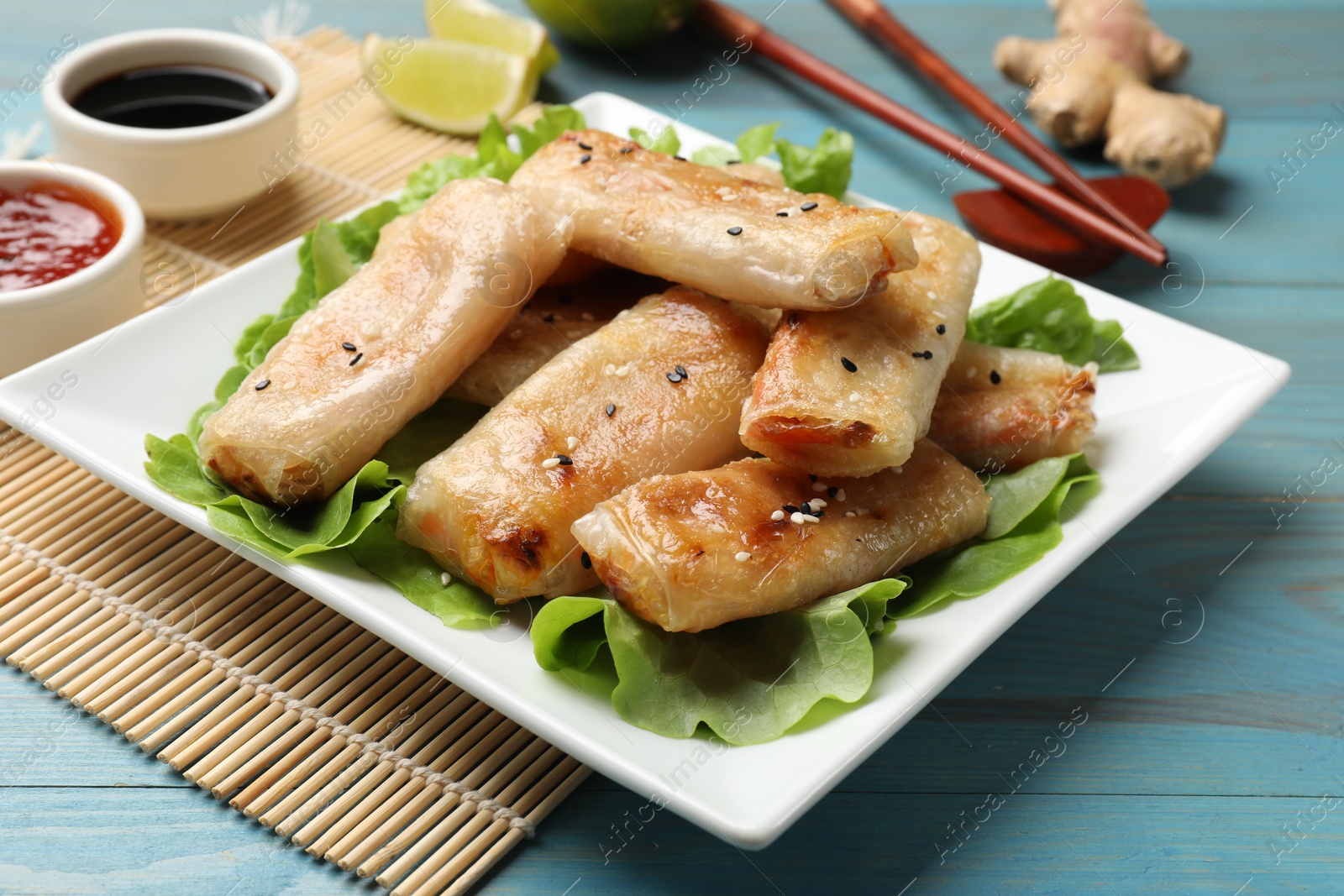 Photo of Tasty fried spring rolls and lettuce on light blue wooden table, closeup