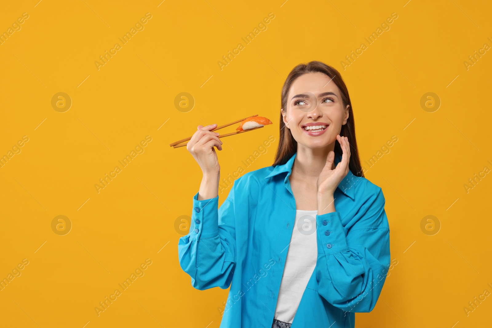 Photo of Happy beautiful young woman holding sushi with chopsticks on orange background. Space for text