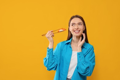Photo of Happy beautiful young woman holding sushi with chopsticks on orange background. Space for text