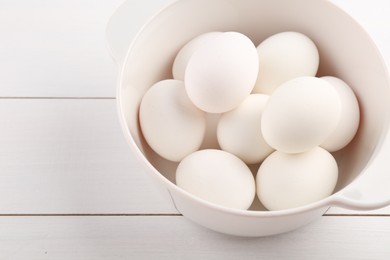 Photo of Boiled eggs in saucepan on white wooden table, closeup. Space for text