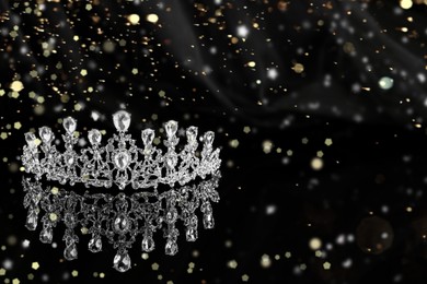 Image of Beautiful silver tiara with diamonds on dark mirror surface, space for text. Bokeh effect