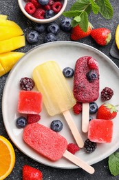 Photo of Plate of different tasty ice pops on black textured table, flat lay. Fruit popsicle