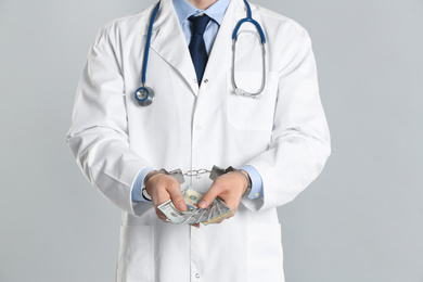 Photo of Doctor in handcuffs with bribe on grey background, closeup. Corrupted medicine