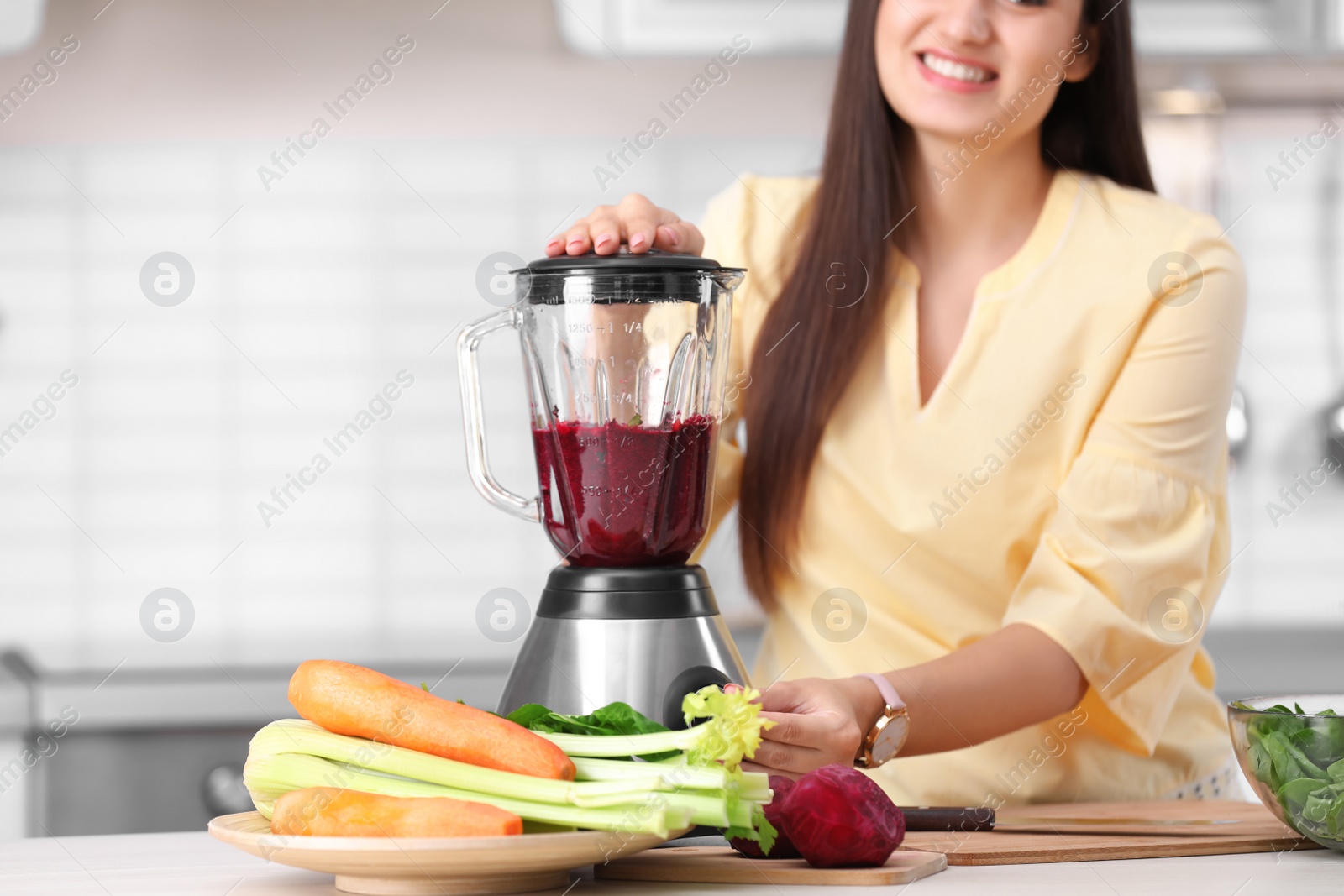 Photo of Young woman preparing tasty healthy smoothie at table in kitchen