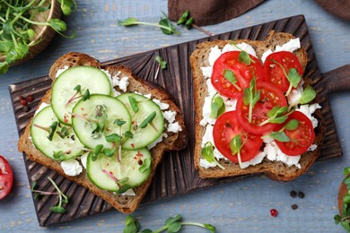 Delicious sandwiches with vegetables, cheese and microgreens on grey wooden table, flat lay